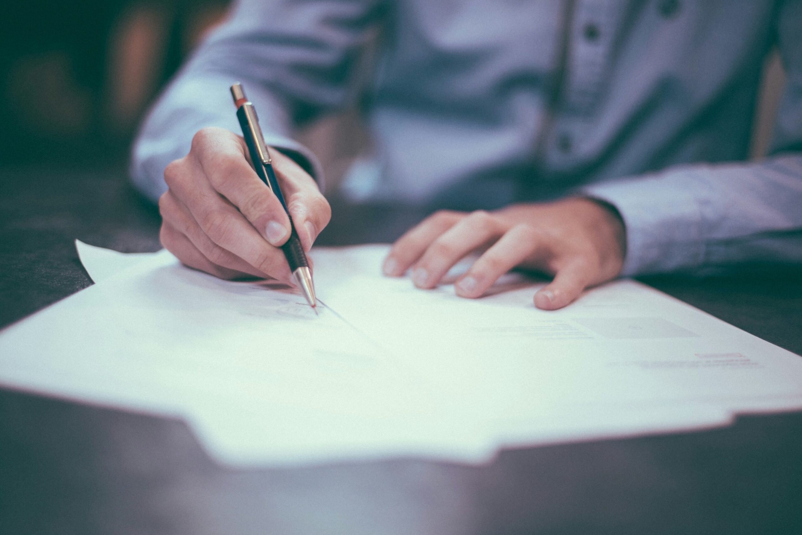 A hand holding a pen and writing on a piece of paper